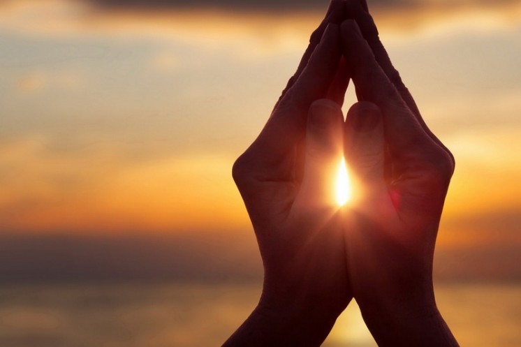 Zwei Hände beten zusammengefaltet vor einem schönen Sonnenuntergang im Wellnesshotel in Ruhpolding
