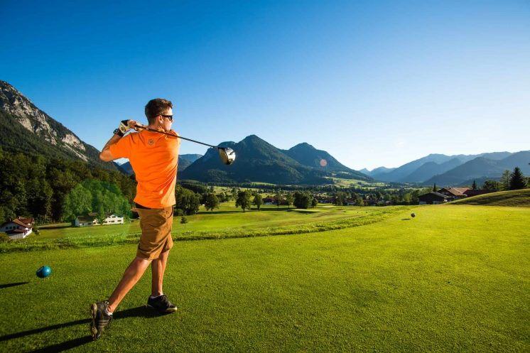 Ein Mann schlägt einen Ball auf einem grünen Golfplatz während seinem Wochenendurlaub in Bayern