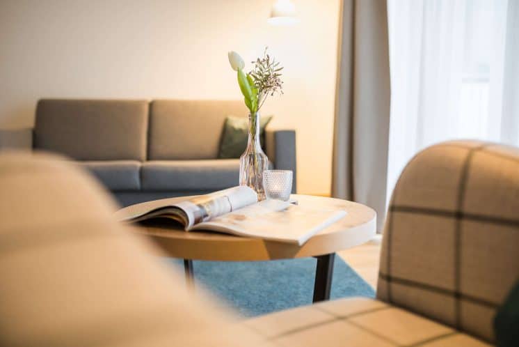 helds-vitalhotel-ruhpolding-zimmer_heldenparadies Nahaufnahme eines runden Beistelltisches neben einer Sitzecke mit Sofas